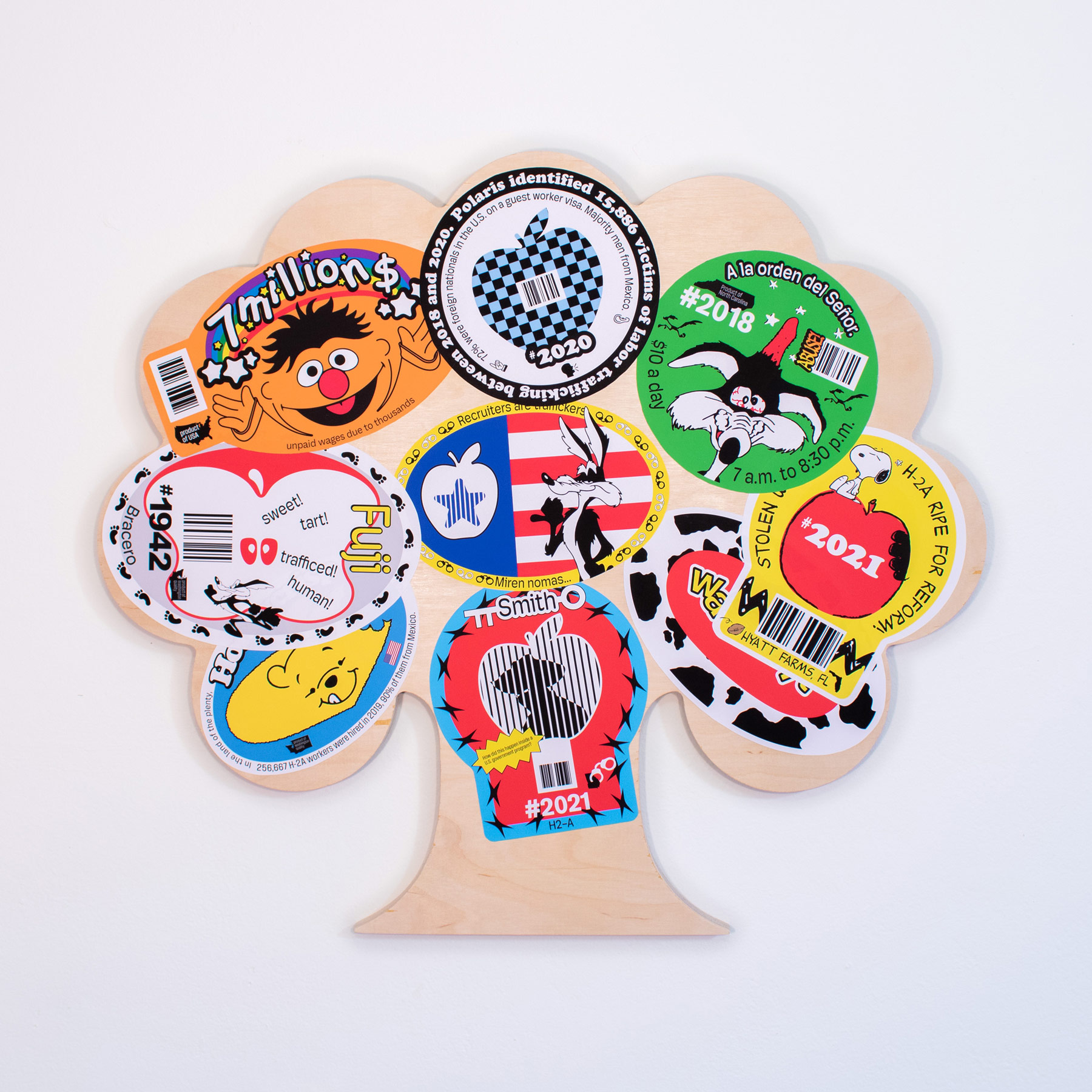 A poster made of a wooden tree with various stickers depicting different themes, including labor rights, immigration, and social issues. The stickers feature characters from popular culture and informative text.