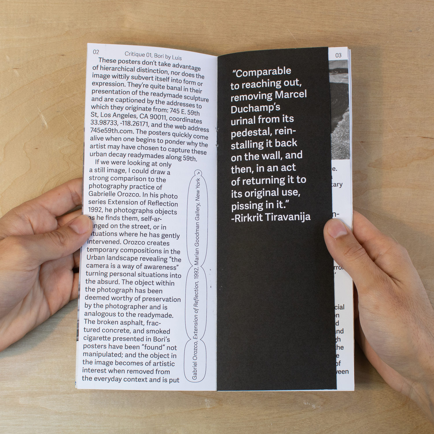 hands holding open a zine of a critical review of Bori Jiang, cover features an image of a street in los angeles with the title centered towards the top in black and white over a wood panel background